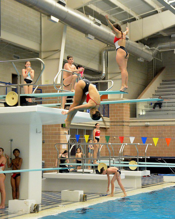competitive divers training during summer camp, one diver is mid air in a somersault and others are on the board